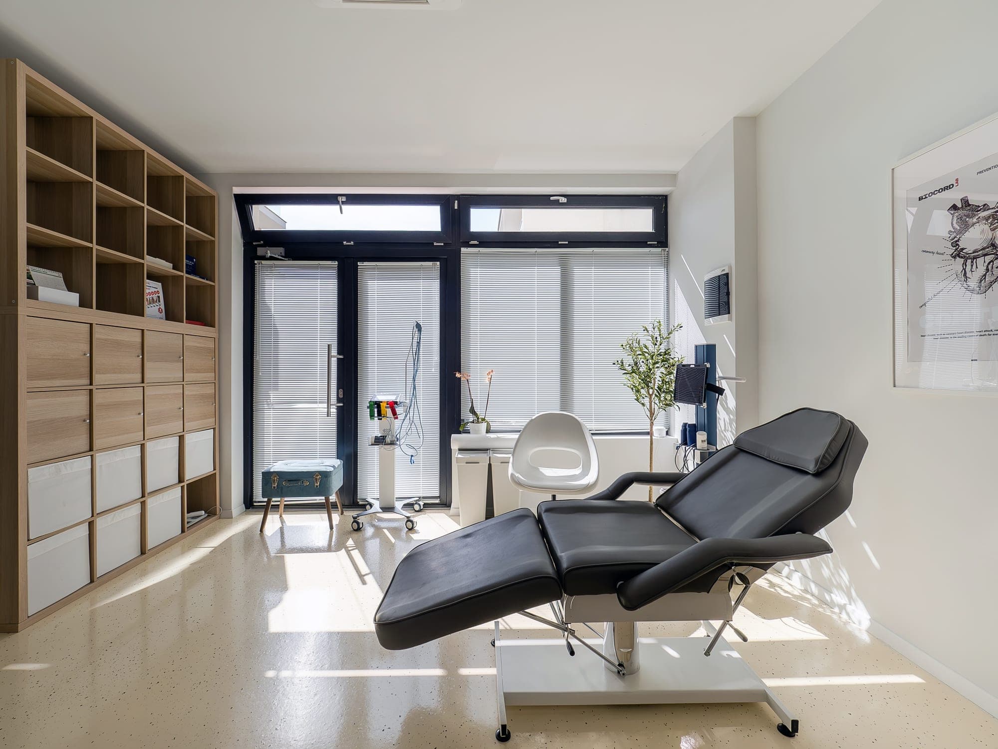 The consulting room, with the examination couch, wooden shelving and large windows